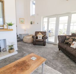 A living room with a wood burning stove armchair sofa coffee table and glass doors leading to another room at Minerva in Trearddur Bay