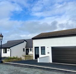A white house with black doors and windows a garage door and a street lamp outside at Minerva in Trearddur Bay