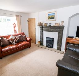 A living room with two leather sofas a decorative fireplace a television on a wooden stand and a window at Manor Farm Cottage in Swaffham