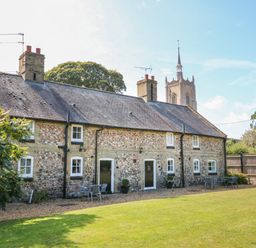 A row of stone cottages with outdoor seating and a grassy lawn at Manor Farm Cottage in Swaffham
