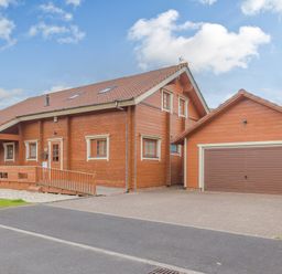 A wooden house with a tiled roof and attached garage with driveway at Jamaal Lodge in South Broomhill near Amble