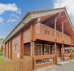 A wooden house with a covered porch and balcony in a residential area at Jamaal Lodge in South Broomhill near Amble