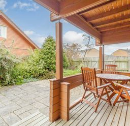 A covered wooden patio with a round table and four chairs overlooking a garden with bushes and wooden fences at Jamaal Lodge South Broomhill near Amble