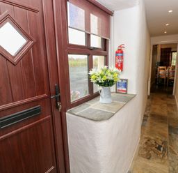 A hallway with a wooden front door a window with a flower vase on the sill and a fire extinguisher at Potters Barn in Begelly near Kilgetty