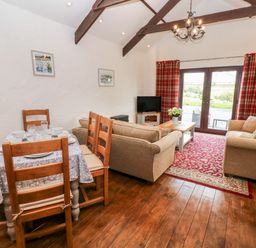 A living room with two sofas a dining table and chairs wooden floor and red curtains at Potters Barn in Begelly near Kilgetty