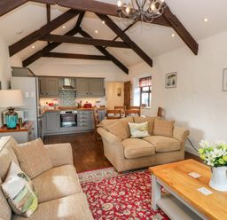 A living room with beige sofas wooden beams kitchen and dining area at Potters Barn in Begelly near Kilgetty