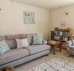 A living room with a gray sofa and cushions a wooden coffee table a wooden bookshelf an armchair and a floor lamp at Megs Cottage in Norwich