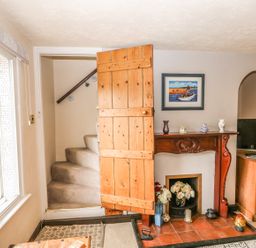A room with a wooden door open to carpeted stairs a fireplace with decorative items a television on a wooden cabinet and a window with a view outside at Megs Cottage Norwich
