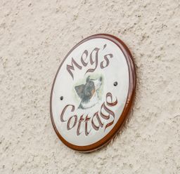 A circular sign on a textured wall with the text Megs Cottage and an illustration of a dog at Megs Cottage in Norwich