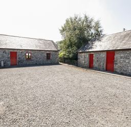 A gravel courtyard between two stone buildings with red doors and windows at The Visiting House in Gorteen near Dunmore County Galway