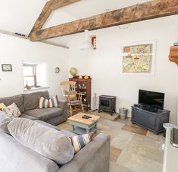 A living room with gray sofas wooden beams a rocking chair a small fireplace and a television at The Visiting House in Gorteen near Dunmore County Galway