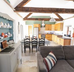 A kitchen and dining area with wooden cabinets a dining table with chairs and a gray sofa with a striped pillow at The Visiting House in Gorteen near Dunmore County Galway