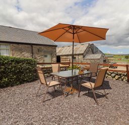 An outdoor patio area with a table and four chairs under an orange umbrella next to stone buildings at Y Bwthyn in Ysbyty Ifan