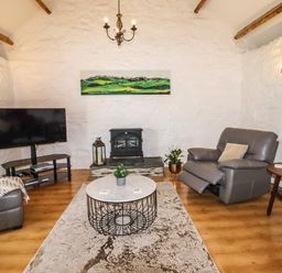 A living room with a grey recliner chair a round coffee table a television on a stand a wooden side table and a fireplace at Y Bwthyn in Ysbyty Ifan