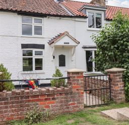 A white brick cottage with a tiled roof a small garden with two chairs a table a brick wall and a metal gate at The Cottage Kilham near Driffield