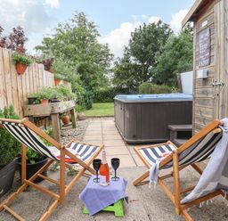 A garden patio with two wooden deck chairs and a small table with glasses and a bottle near a hot tub at The Cottage in Kilham near Driffield