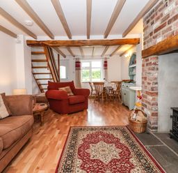 A living room with wooden beams a red and beige rug and a brick fireplace at The Cottage Kilham near Driffield