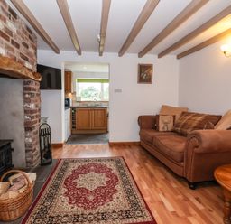 A living room with a brown sofa and round wooden table next to a brick fireplace and a rug on the floor at The Cottage in Kilham near Driffield