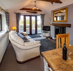 A living room with cream sofa wooden dining table and glass doors leading to a patio at Cwm Derw Cottage in Llanafan Fawr near Builth Wells