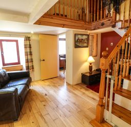 A living room with a brown leather sofa near a window with striped curtains and a wooden staircase with a lamp on a side table at Sutton Cottage in Ballysheen near Rosslare Harbour County Wexford