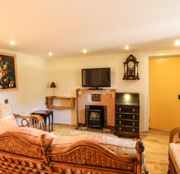 A living room with wicker furniture a wall clock a television above a fireplace and a yellow door at Sutton Cottage in Ballysheen near Rosslare Harbour County Wexford