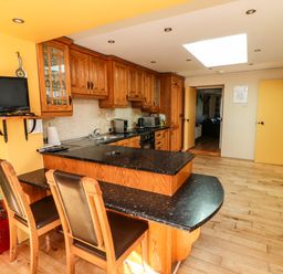 A kitchen with wooden cabinets black countertops a small TV and two chairs at Sutton Cottage Ballysheen near Rosslare Harbour County Wexford