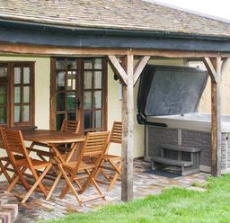 An outdoor covered patio with wooden table and chairs and a hot tub at Brambles Cottage in Little Malvern near Malvern