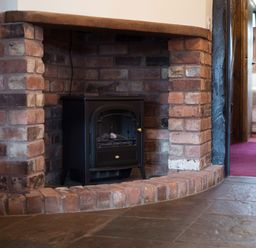 A brick fireplace with a black stove inside and a tiled floor at Brambles Cottage in Little Malvern near Malvern
