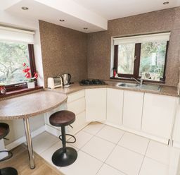 A kitchen with a countertop stove sink toaster kettle two stools and two windows at The Garden Flat in Saundersfoot