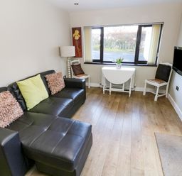A living room with a black leather sofa and cushions a small folding table with a vase near a window and two white chairs at The Garden Flat in Saundersfoot