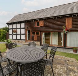 A round outdoor metal table with six chairs on a stone patio next to a timber and black and white painted building at Stable End in Luntley near Pembridge