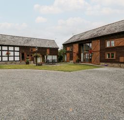 Two barn style buildings with wooden cladding and stone foundations a gravel courtyard and a lawn area with outdoor furniture at Stable End in Luntley near Pembridge
