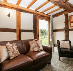 A sitting area with a brown leather sofa and armchair near a door with exposed wooden beams on walls and ceiling at Stable End in Luntley near Pembridge