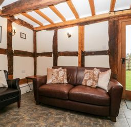A sitting area with a brown leather sofa, black armchair, side table, wall lights, and a door opening to a garden at Stable End in Luntley near Pembridge