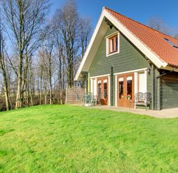 A green wooden house with a red roof next to a grassy yard and trees at Apple Tree Lodge in Swarland near Alnwick