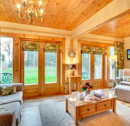 A living room with wooden ceiling and large windows showing greenery outside at Apple Tree Lodge Swarland near Alnwick