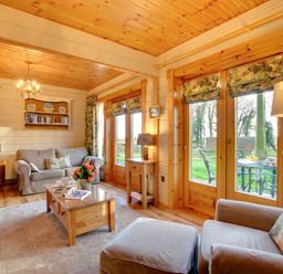 A living room with sofas coffee table lamp bookshelf and windows showing garden at Apple Tree Lodge Swarland near Alnwick