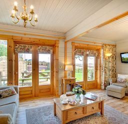 A living room with wooden framed glass doors sofa armchair coffee table with tea set and flowers at Lime Tree Lodge Swarland near Alnwick