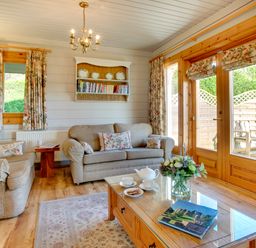 A living room with sofas a coffee table with tea set and flowers and wooden doors at Lime Tree Lodge Swarland near Alnwick