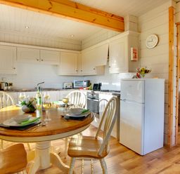 A kitchen with a wooden dining table set for four with wine glasses and white cabinets at Lime Tree Lodge in Swarland near Alnwick