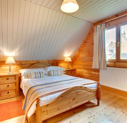 A bedroom with a wooden bed and nightstands with lamps at Lime Tree Lodge in Swarland near Alnwick