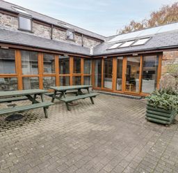 An outdoor patio area with two green picnic tables and wooden framed glass doors at Ddol Helyg Barn in Llanrug
