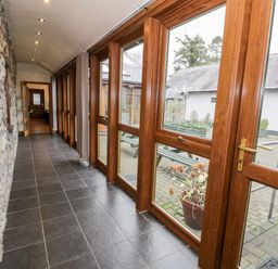 A hallway with stone wall on one side and large wooden framed windows on the other side at Ddol Helyg Barn in Llanrug