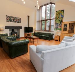 A living room with leather sofas a wooden coffee table TV and large windows at Ddol Helyg Barn in Llanrug