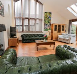 A living room with green leather sofas wood furniture and a fireplace at Ddol Helyg Barn in Llanrug