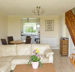 A living room with a beige sectional sofa a wooden coffee table with a flower pot a dining table with four chairs a staircase and a kitchen in the background at Seascope in Kessingland near Lowestoft