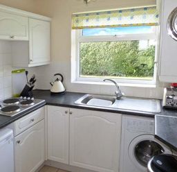 A kitchen with white cabinets a stove microwave kettle toaster and washing machine under a window at Seascope in Kessingland near Lowestoft