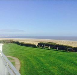 A grassy lawn with a pathway and a view of a sandy beach and the sea at Seascope in Kessingland near Lowestoft