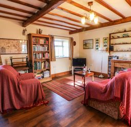 A living room with two armchairs covered with red throws a wooden bookshelf a small coffee table and a television at Cherry Tree Cottage Soulby near Kirkby Stephen
