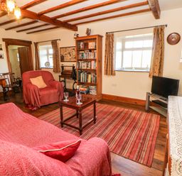 A living room with red covered sofa and armchair wooden bookshelf and striped rug at Cherry Tree Cottage Soulby near Kirkby Stephen